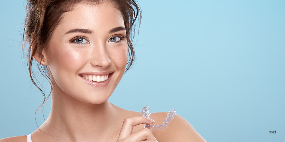 Female holding Invisalign® in her hand on blue background 